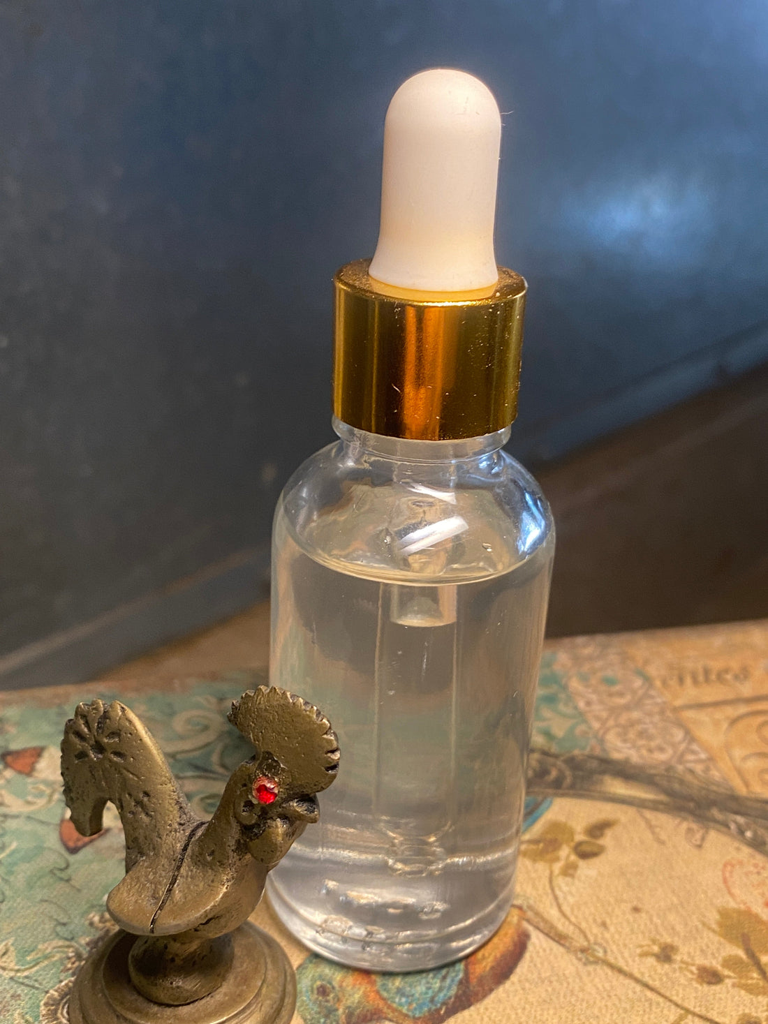 Star Drops Mineral Elixir clear dropper bottle with gold cap beside a small brass rooster against a deep blue background